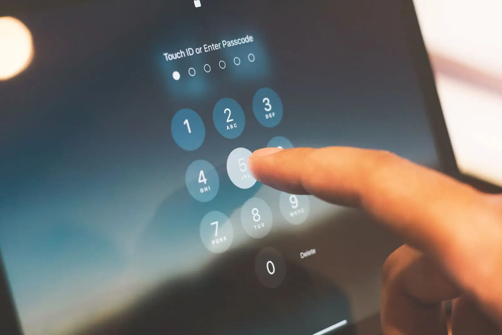Un doigt compose le code sur l'écran de verrouillage d'un appareil Apple, pavé numérique affiché.