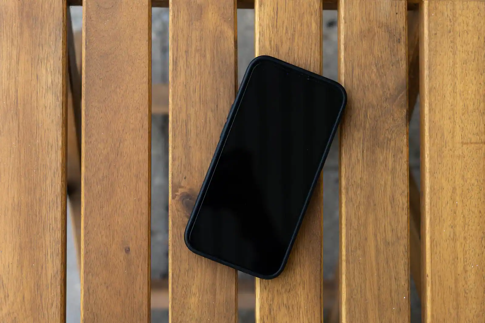 Smartphone posé écran noir sur une table en bois à lames, vu de dessus, appareil visiblement éteint.