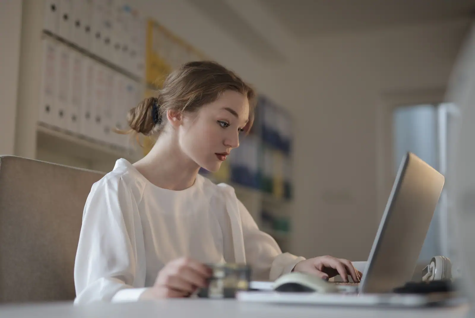 Femme travaillant sur un ordinateur portable dans un bureau, devant des classeurs d'archives.