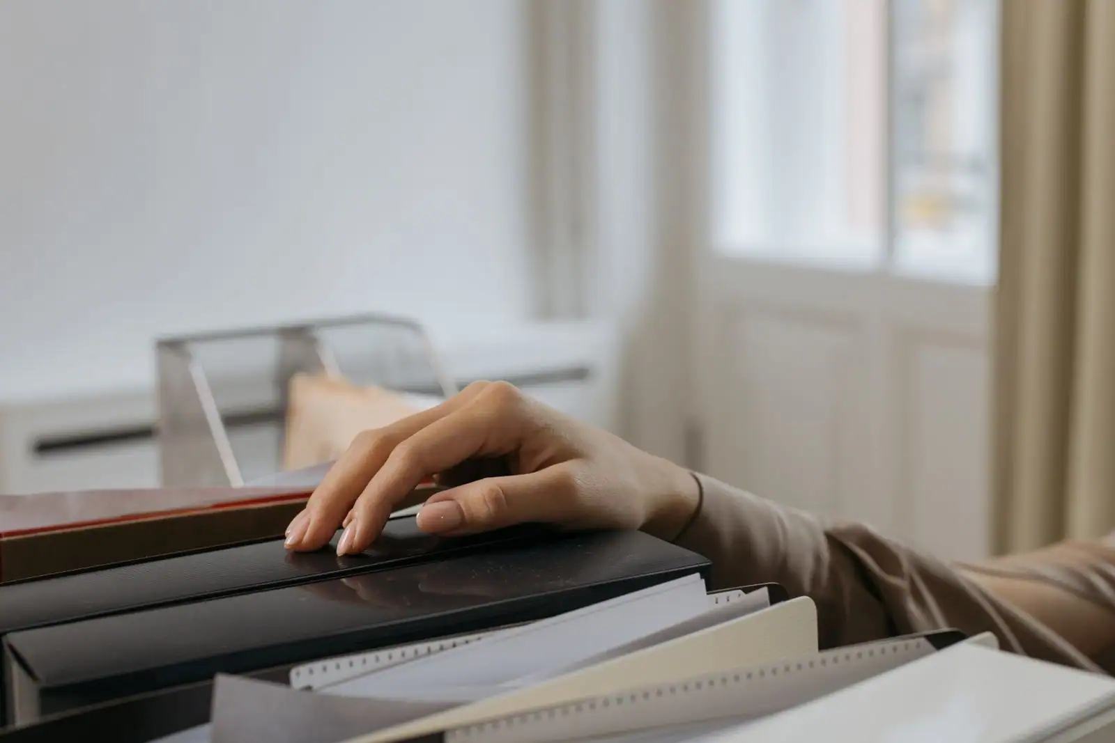 Main posée sur une pile de dossiers et de documents administratifs, dans un bureau clair