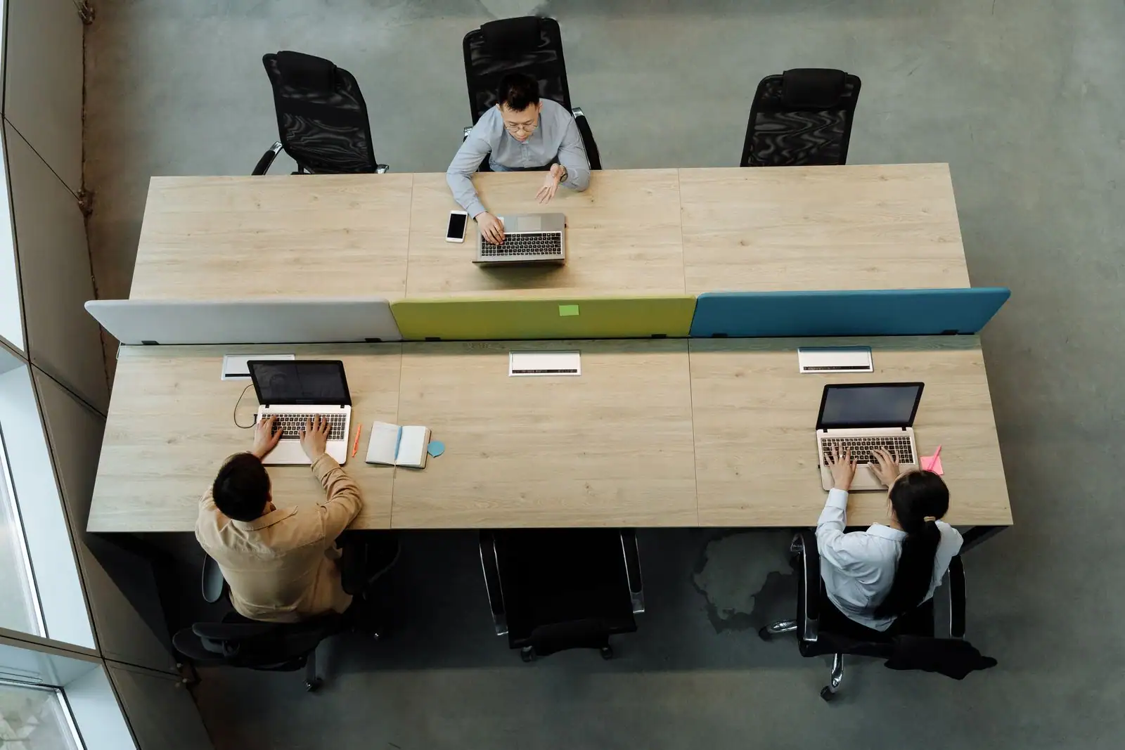 Vue de dessus de trois collègues installés à des bureaux partagés, chacun devant son ordinateur portable.