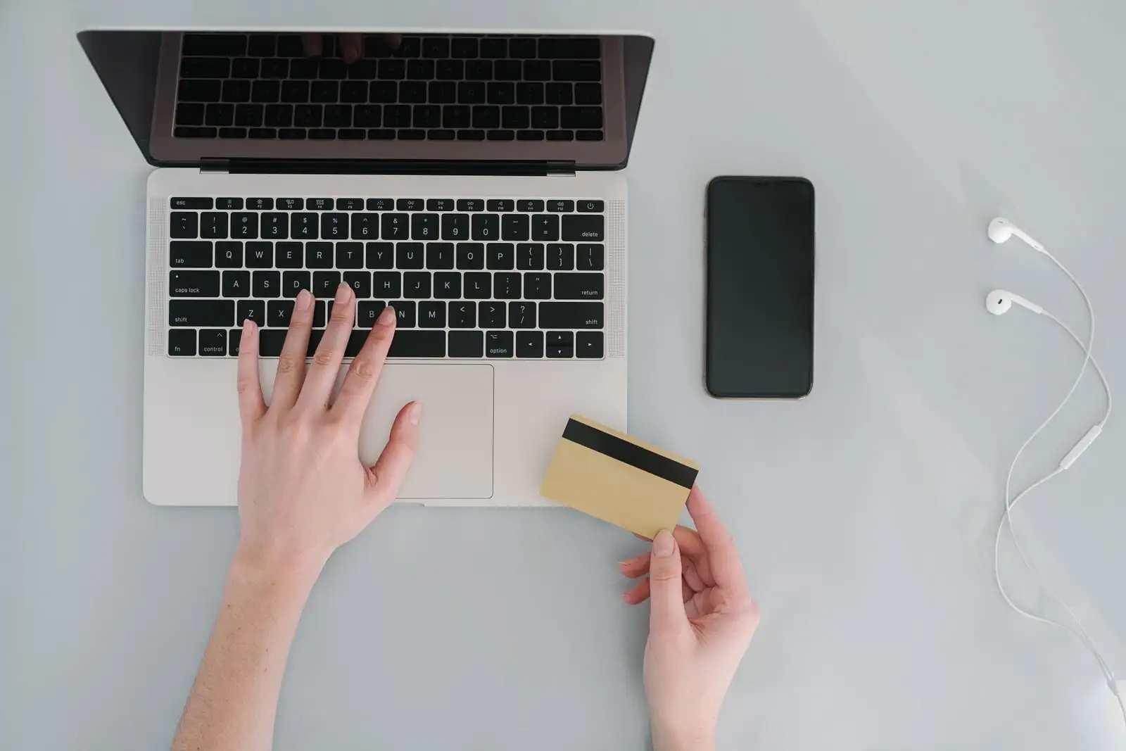 Vue de dessus : mains sur un clavier d'ordinateur portable, carte de paiement et téléphone posés.