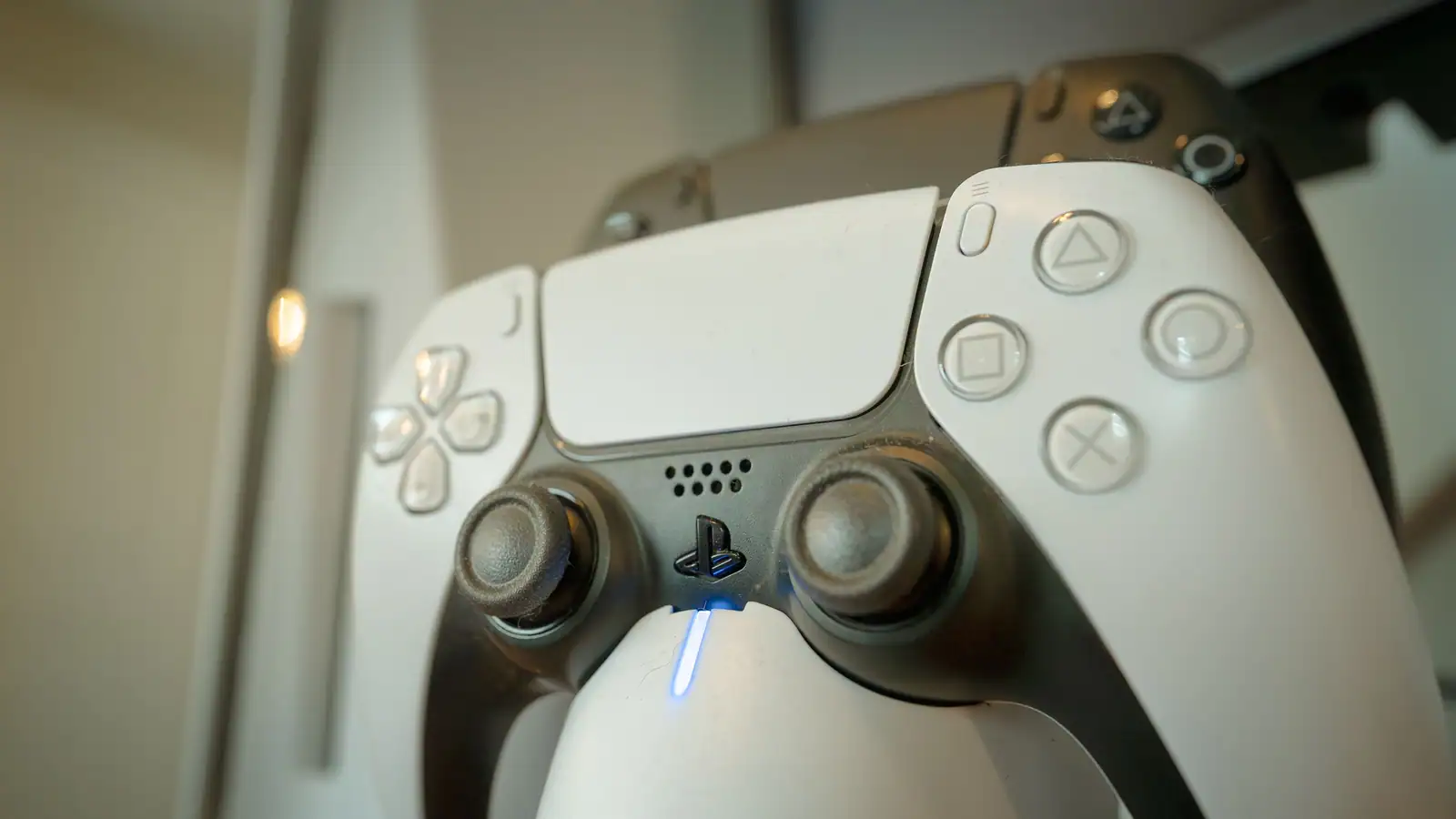 Gros plan sur une manette PlayStation blanche dont la bande lumineuse bleue est allumée, une seconde en arrière-plan