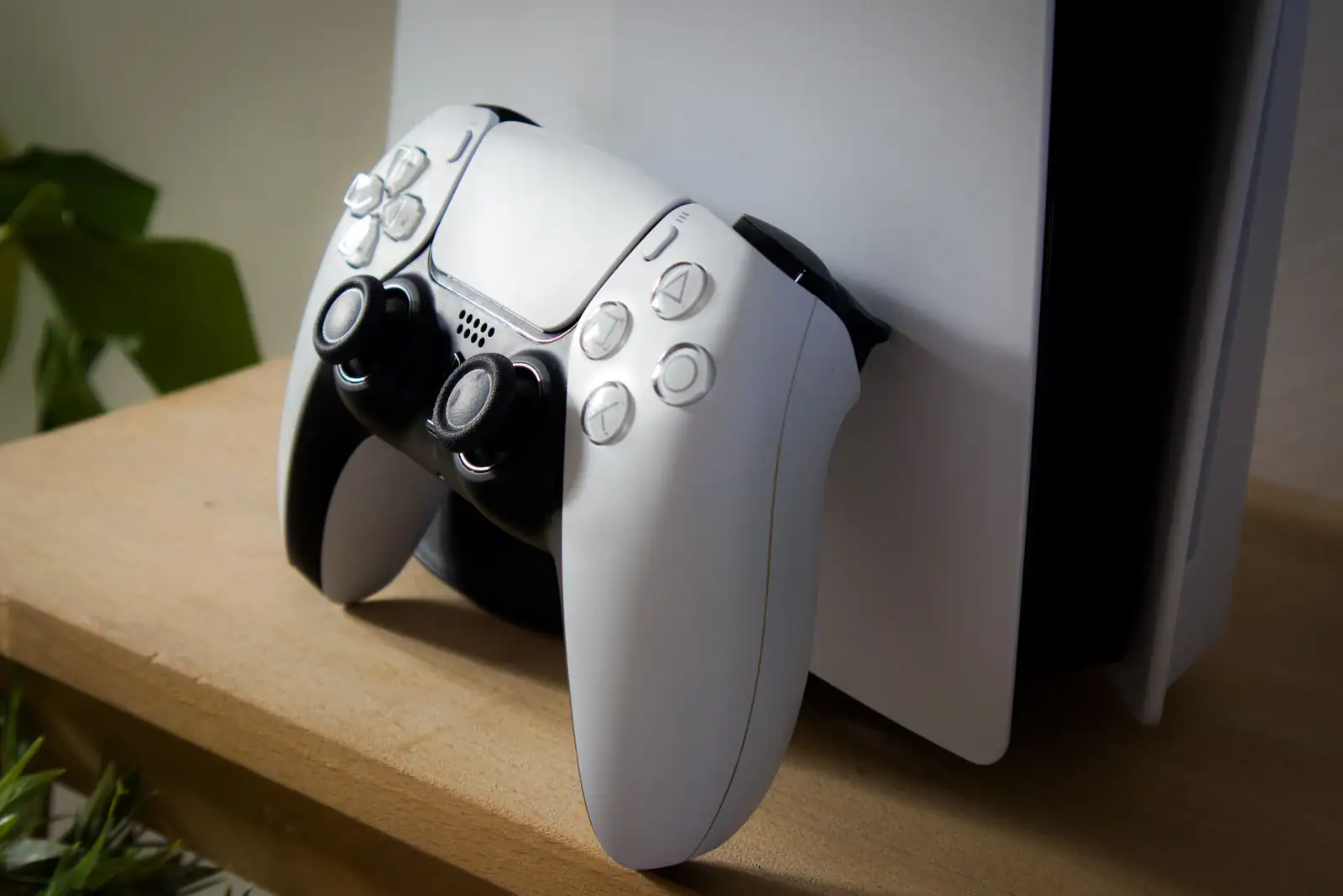 Manette DualSense blanche posée contre une console PlayStation 5 sur une étagère en bois.