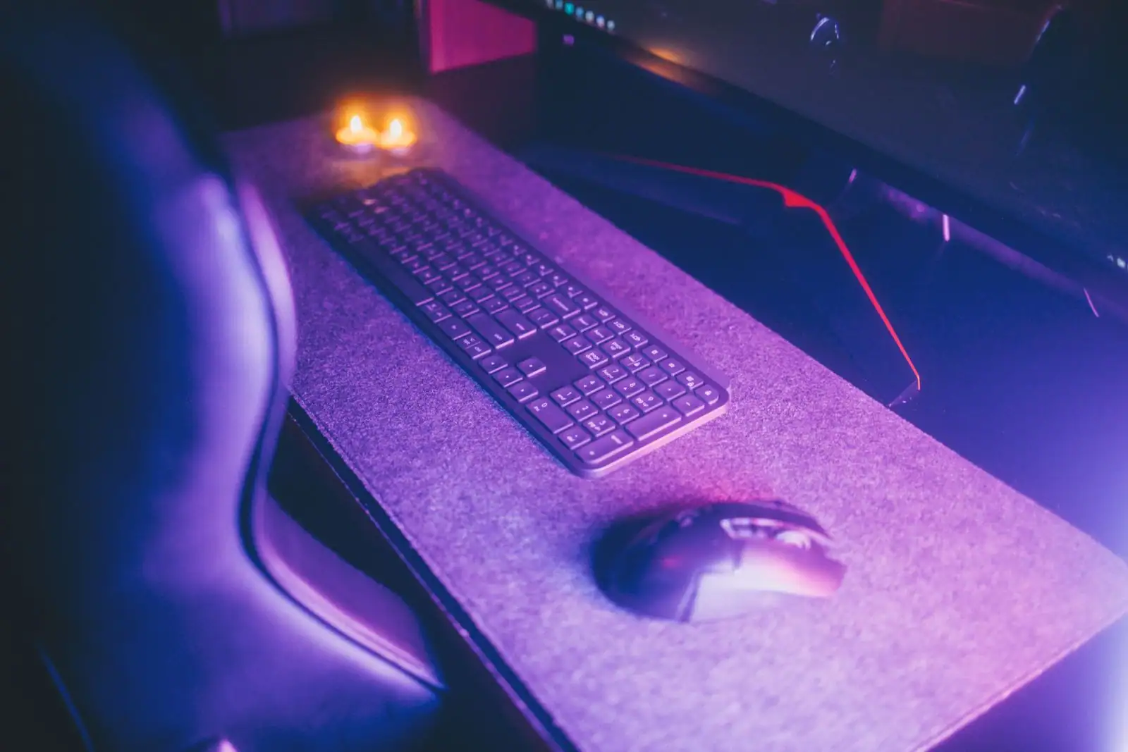 Clavier et souris posés sur un bureau d'ordinateur devant un écran éteint, sous un éclairage violet.
