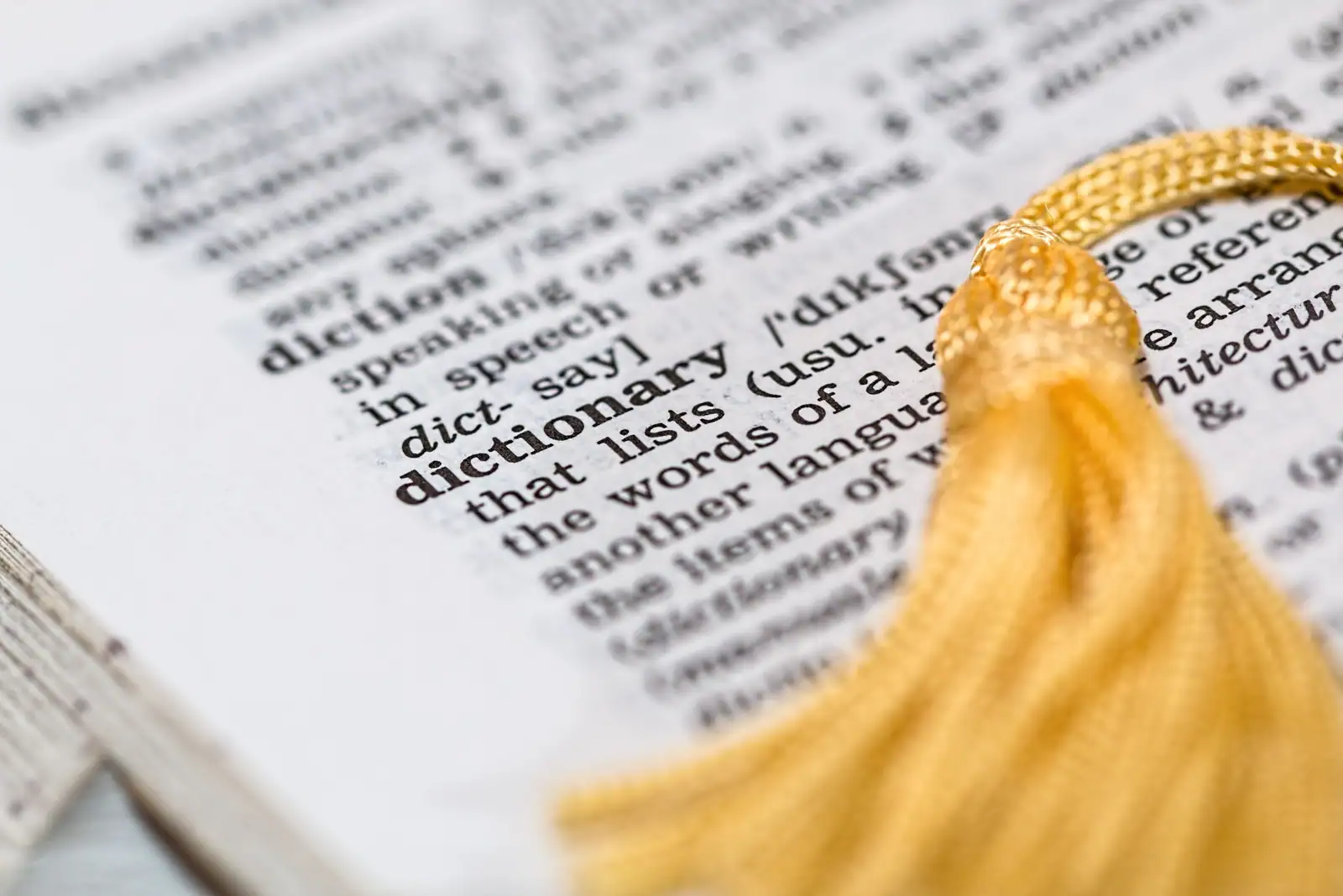 Page de dictionnaire anglais ouverte sur l'entrée « dictionary », avec un marque-page à pompon jaune.
