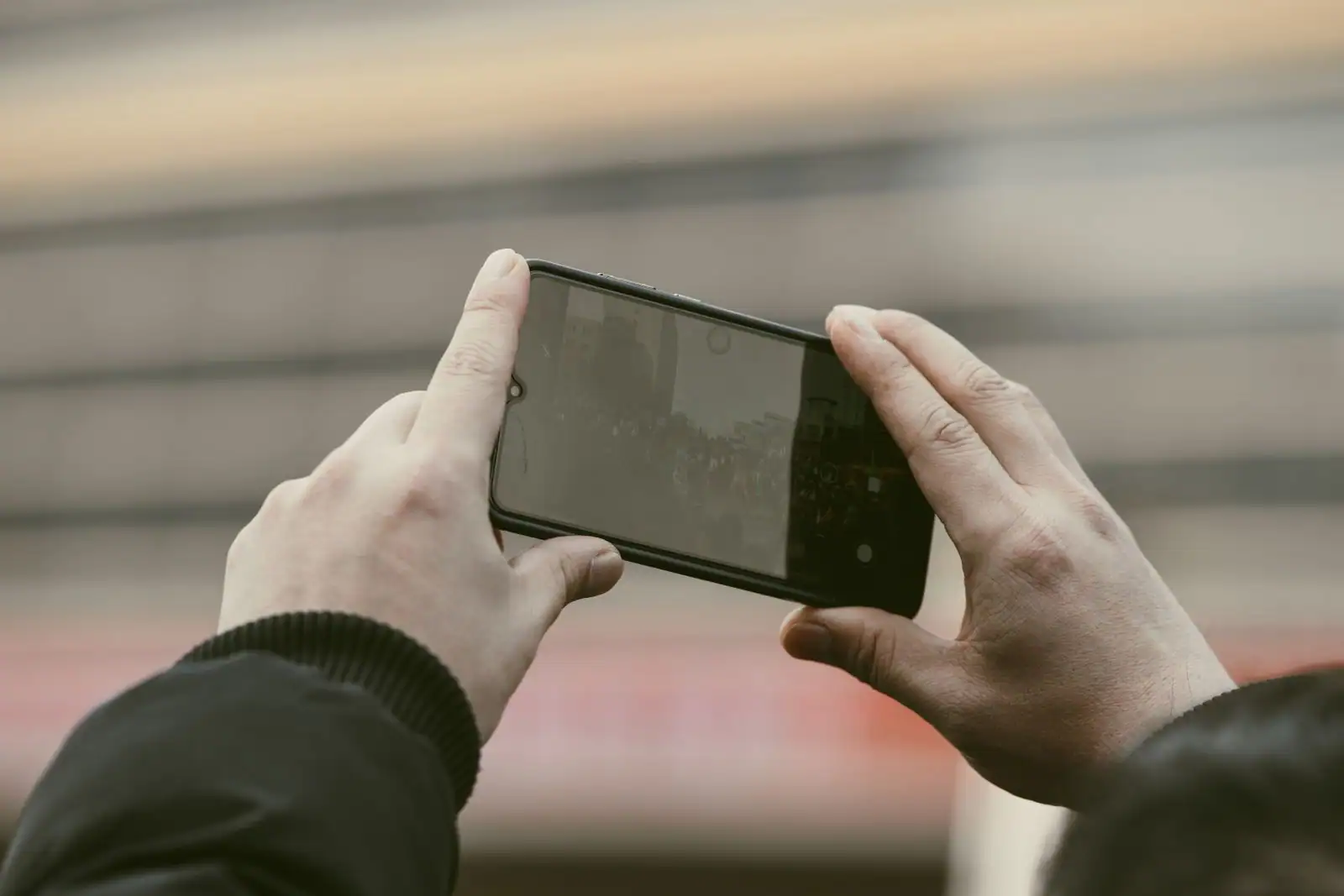 Deux mains tenant un smartphone à l'horizontale, l'écran affichant la scène à photographier.