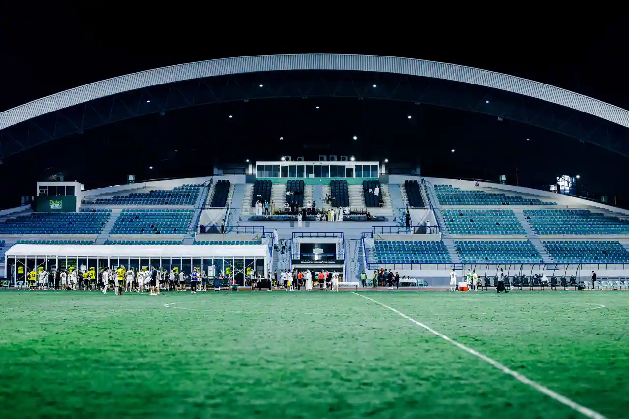 Stade de football éclairé de nuit, tribunes vides et pelouse au premier plan avant la rencontre