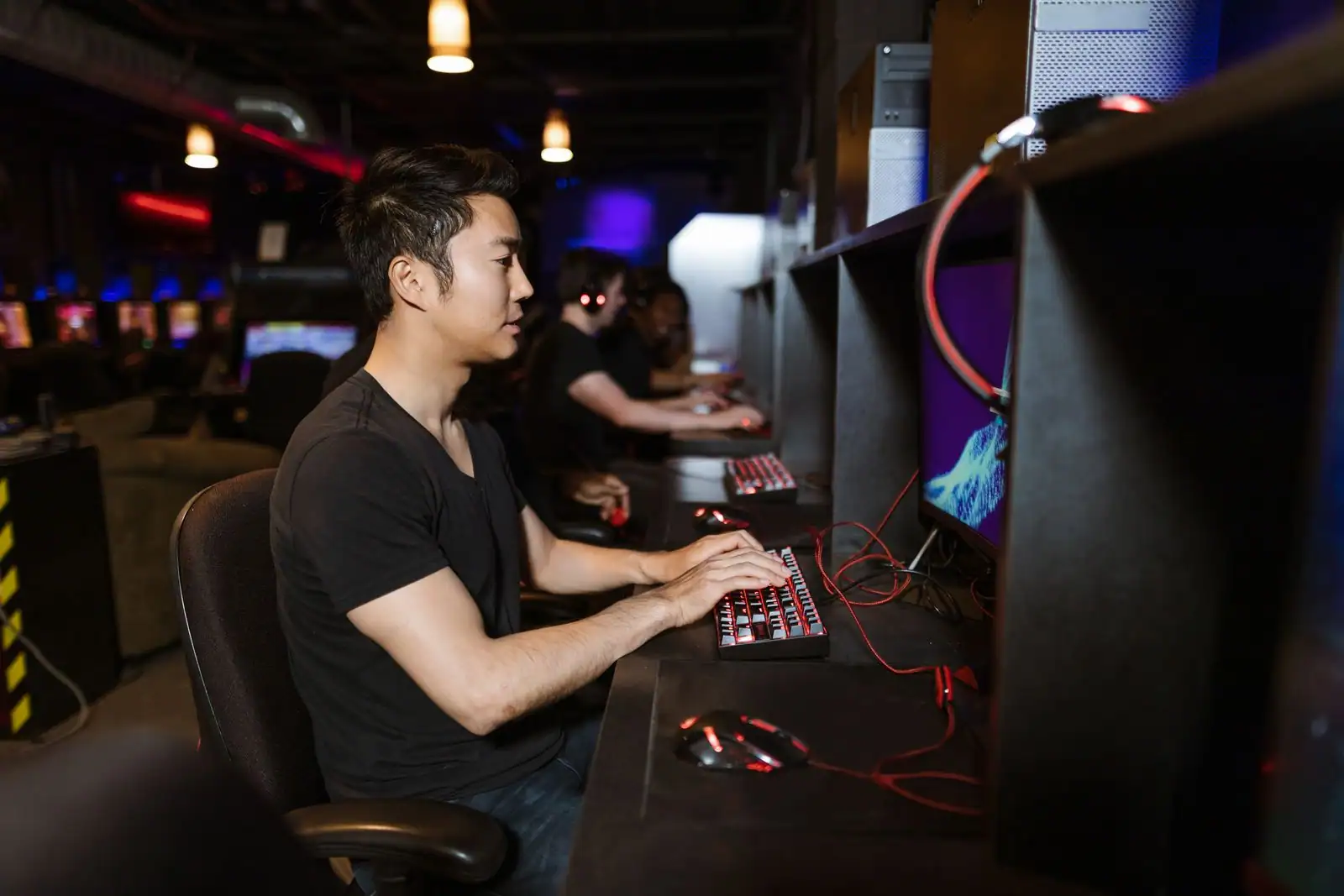 Joueur de profil dans une salle de jeu en réseau, mains sur un clavier d'ordinateur rétroéclairé.