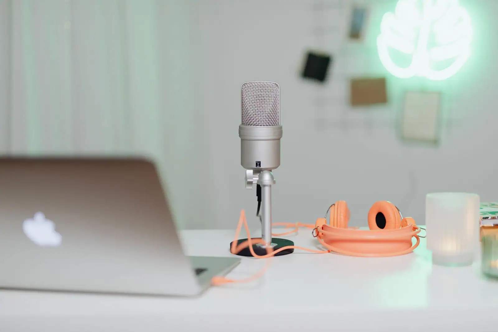 Micro à condensateur sur pied de table, casque orange et ordinateur portable fermé sur un bureau clair.