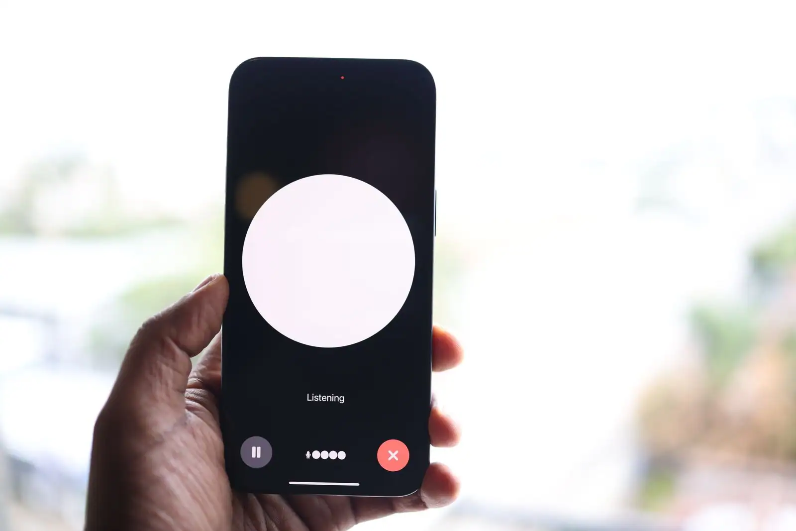 Smartphone tenu en main affichant une interface d'assistant vocal en cours d'écoute.