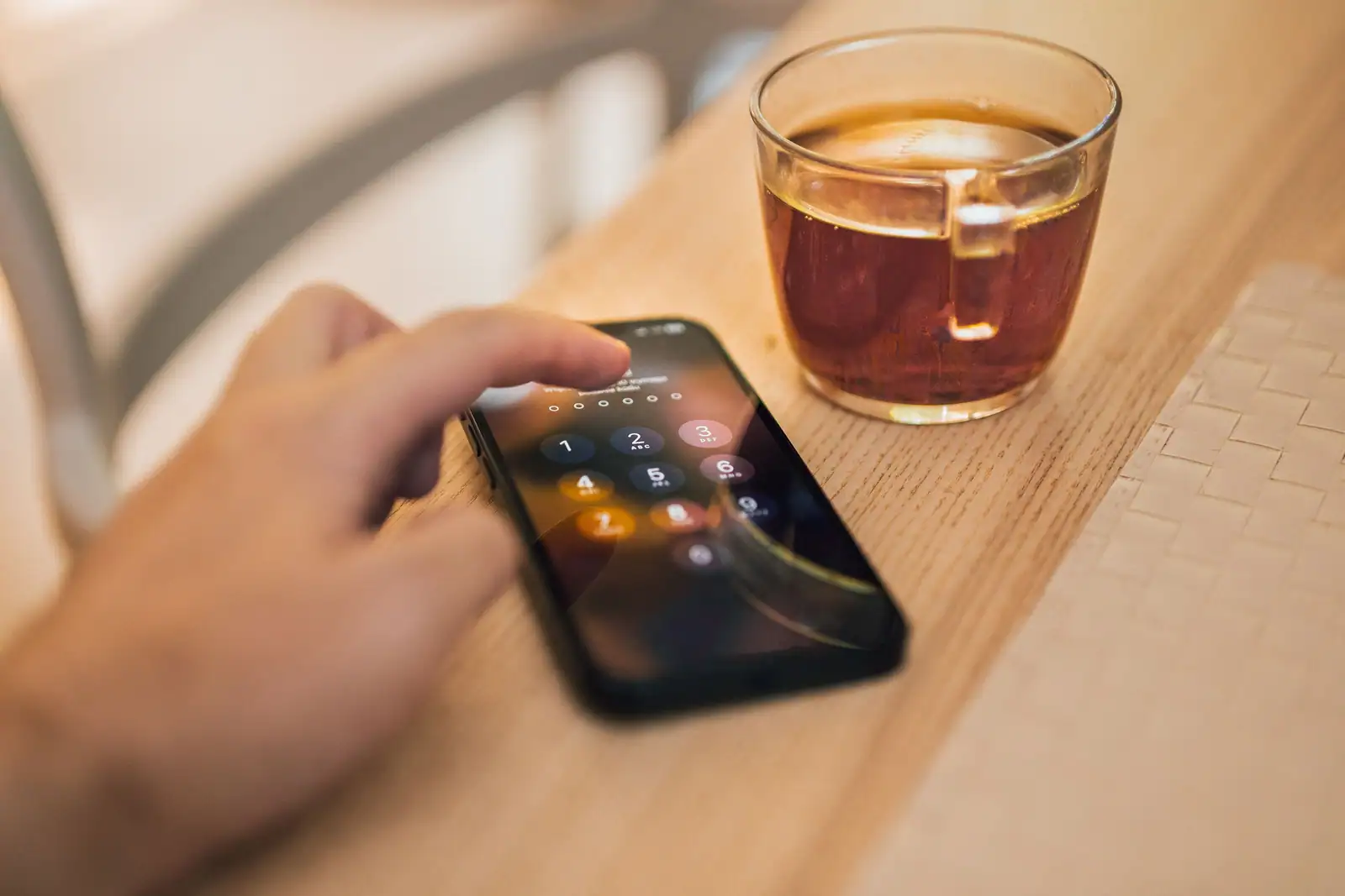 Main entrant un code de déverrouillage sur un smartphone, posé sur une table en bois à côté d'un thé.