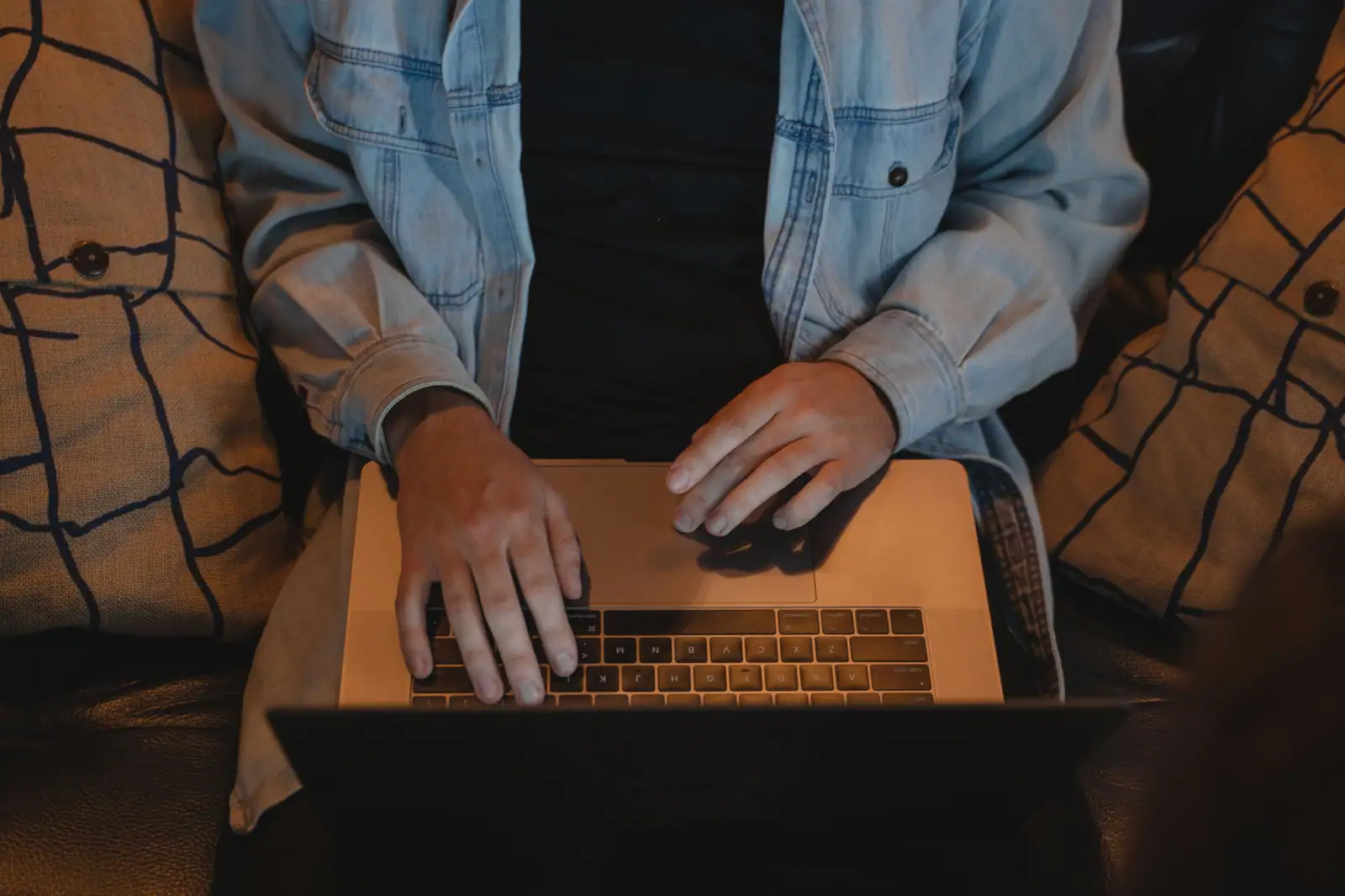 Personne assise, mains posées sur le clavier d'un ordinateur portable, en train de taper.