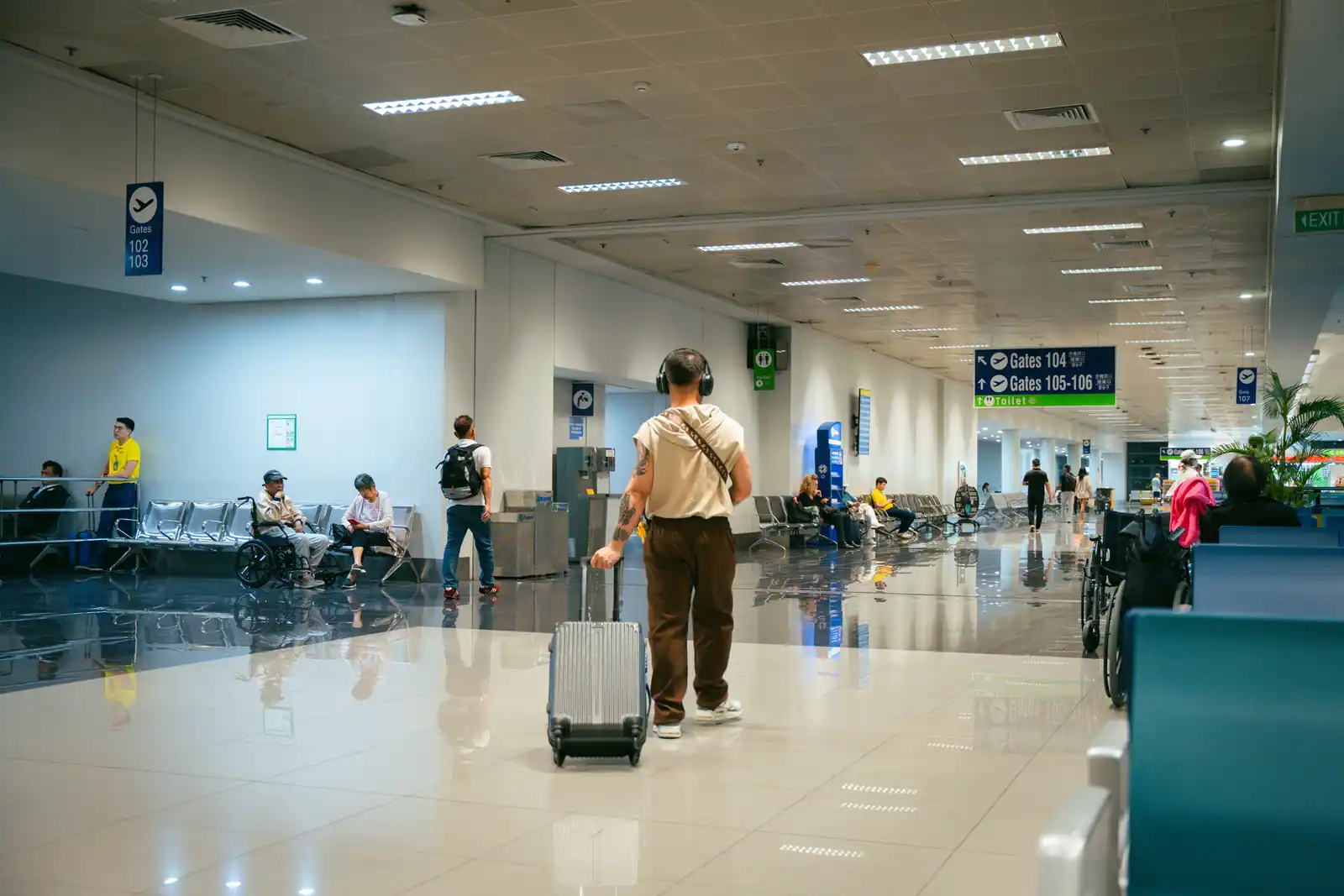 Voyageur avec une valise cabine dans un couloir d'aéroport, panneaux vers les portes d'embarquement