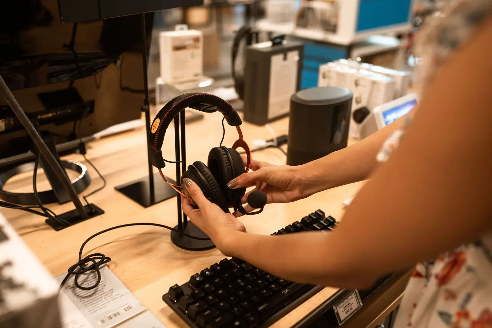 Personne essayant un casque audio exposé sur un présentoir, dans un magasin high-tech.