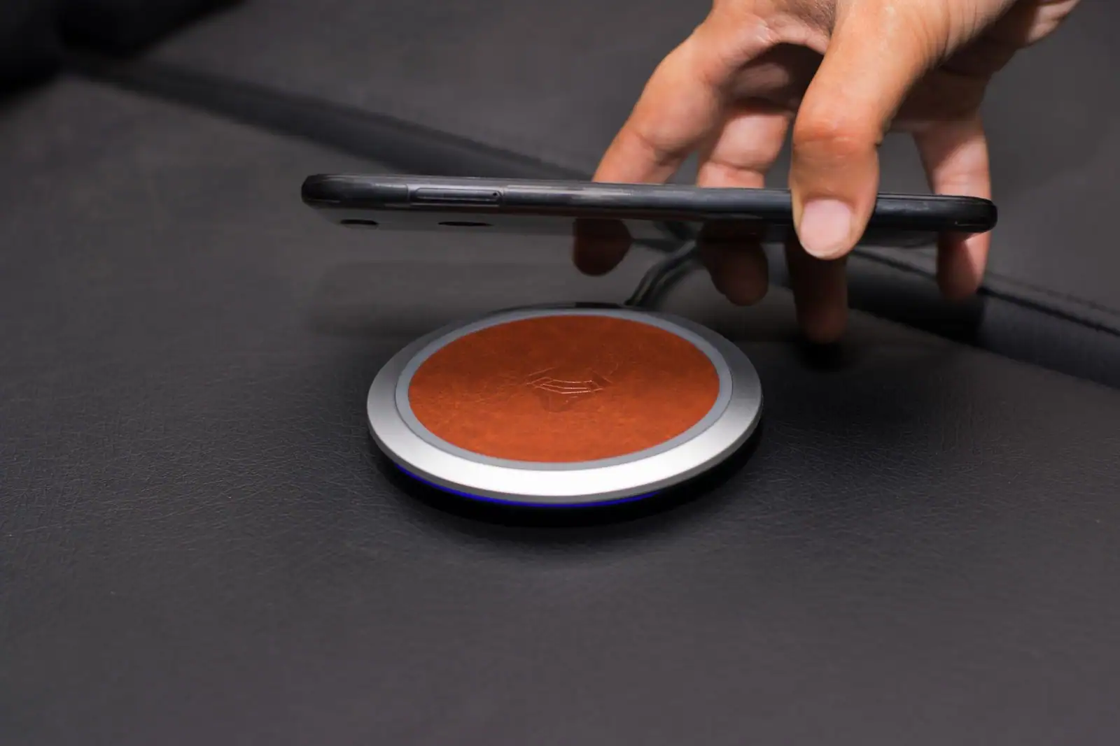 Main posant un smartphone sur un chargeur à induction rond, en cuir et métal.