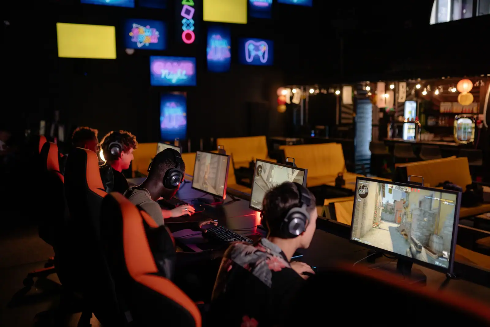 Groupe de joueurs équipés de casques, installés devant plusieurs écrans dans une salle de jeu en réseau.