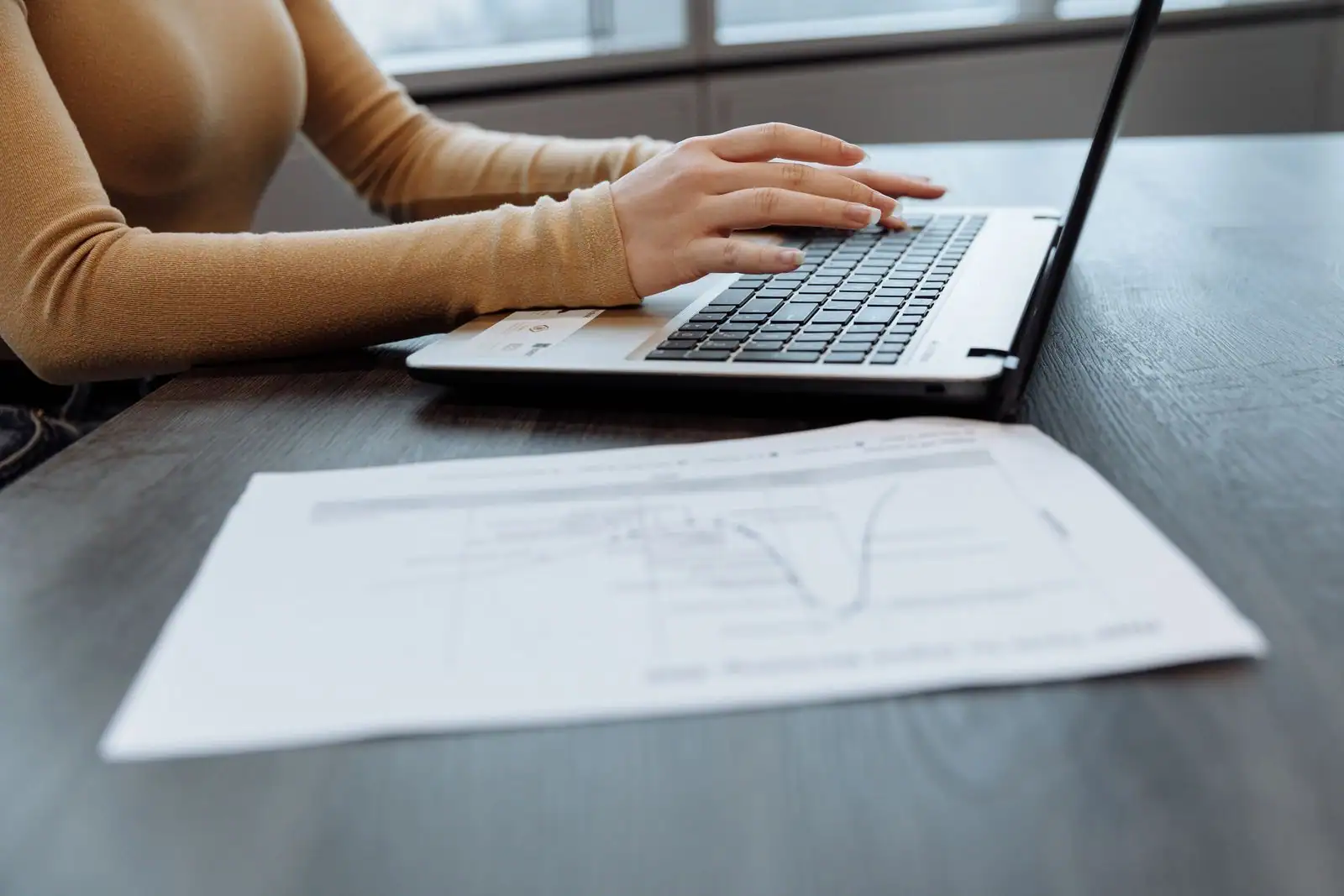 Personne travaillant sur un ordinateur portable, document imprimé à l'appui, dans un contexte professionnel