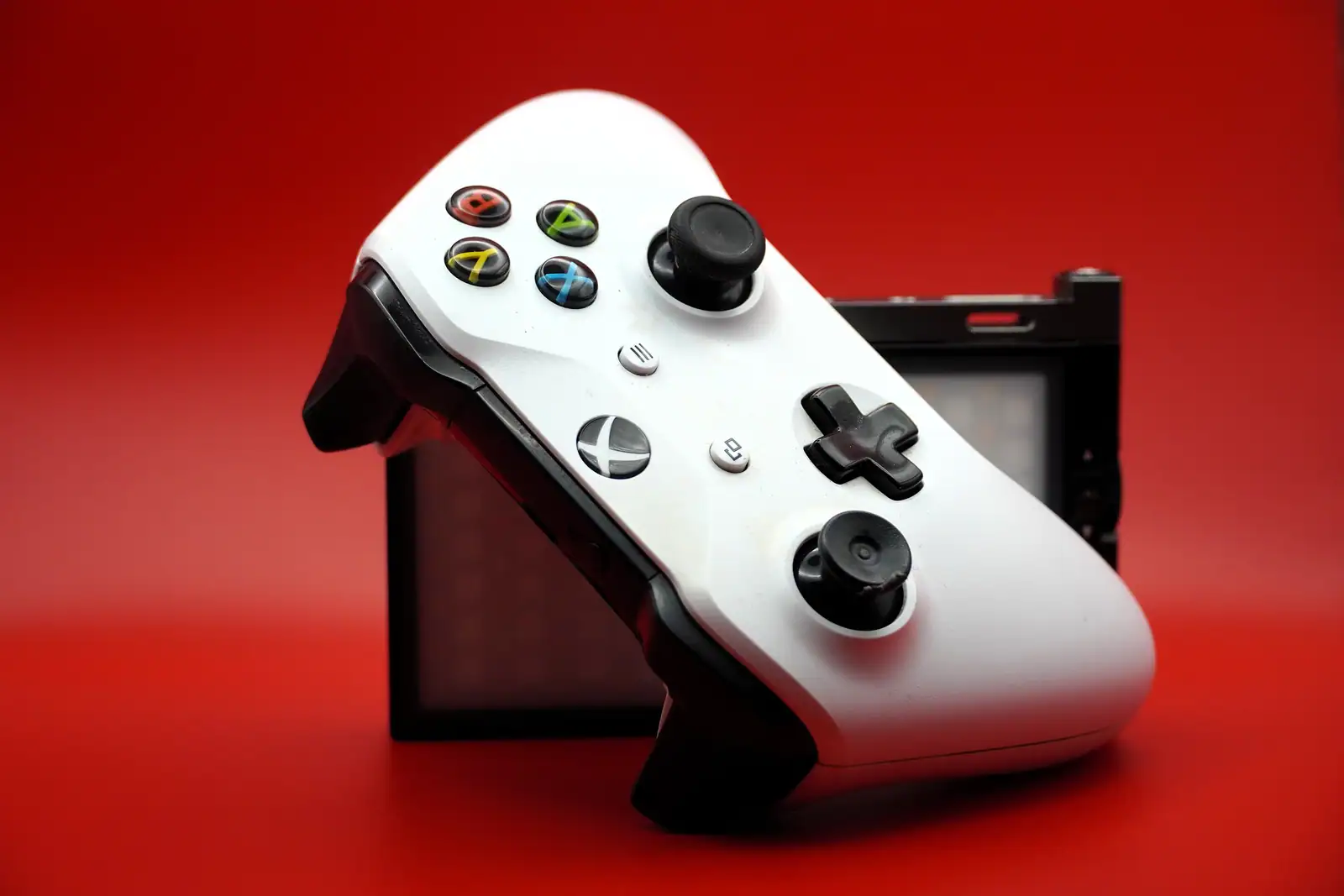 Manette Xbox blanche photographiée en gros plan sur fond rouge vif